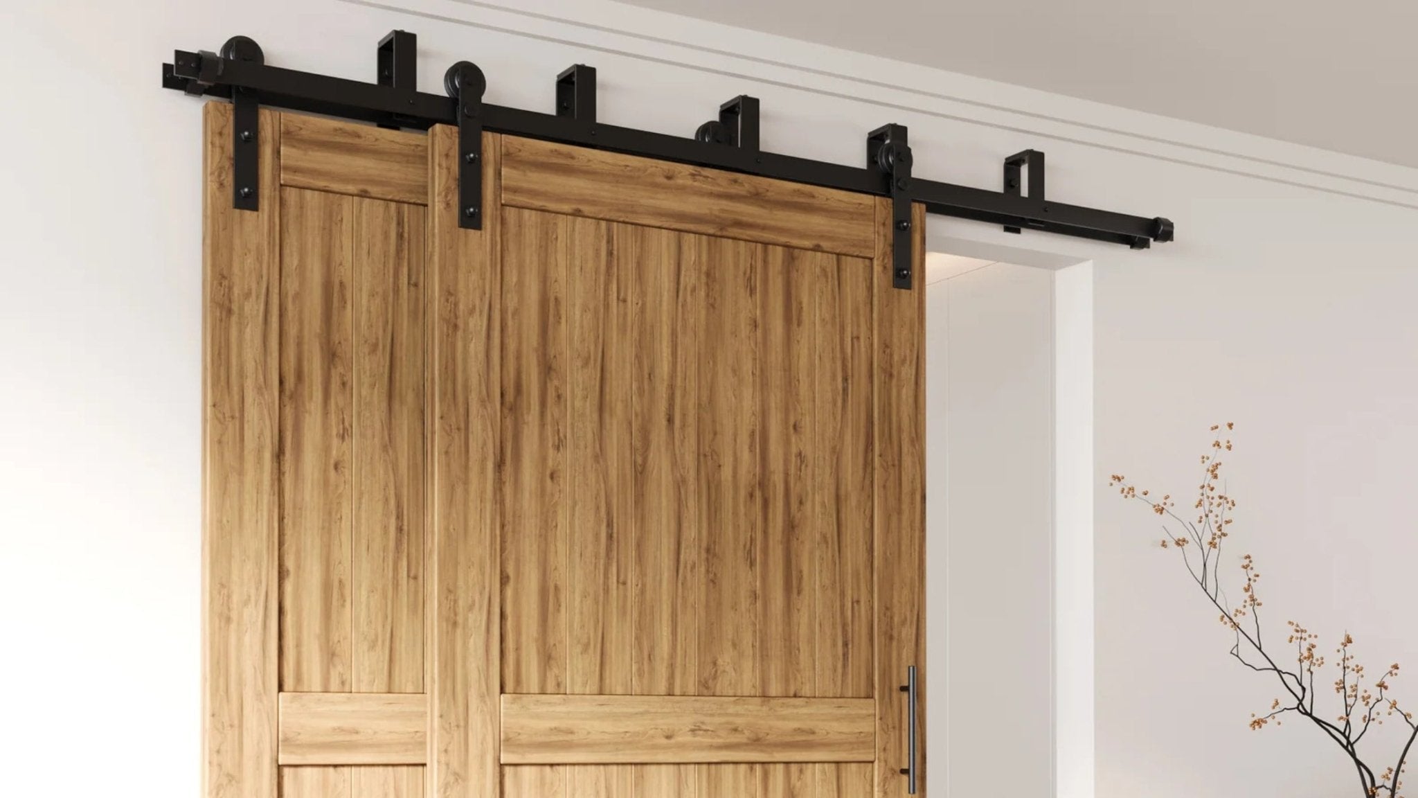 Black double bypass barn door hardware installed on a white wall, supporting two light-colored wooden doors.