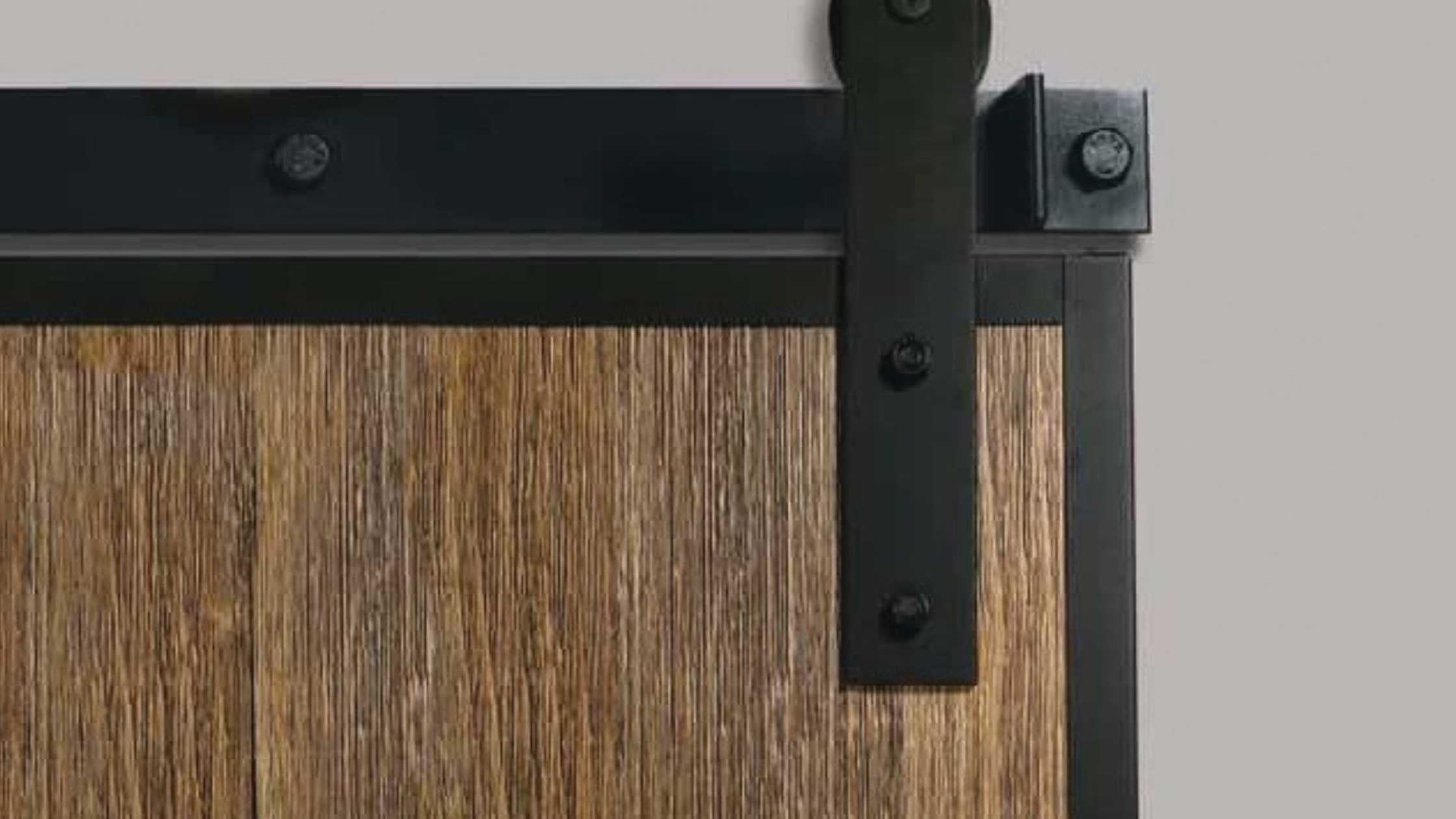 A close-up view of a black edge-wrap barn door hanger bracket and sliding track mounted on a dark stained wood plank door.