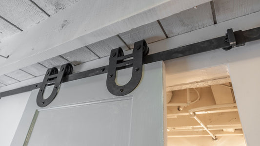 Close-up of black horseshoe-style sliding barn door hardware and track installed on a white wooden door, mounted beneath a white plank ceiling.