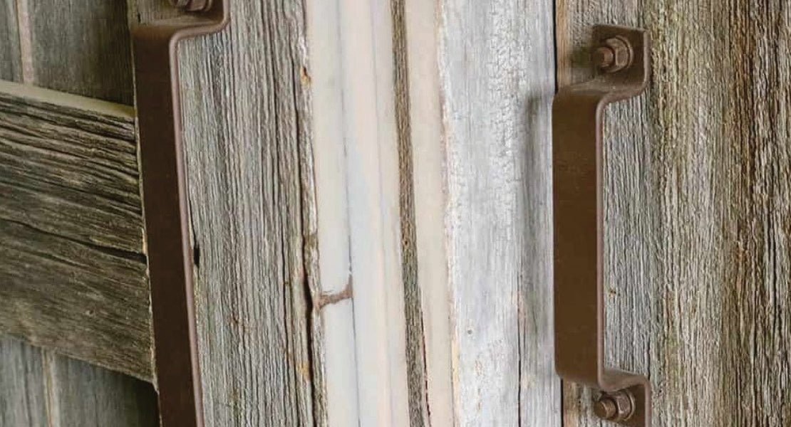 A close up of rustic brown barn door handles on a distressed door.