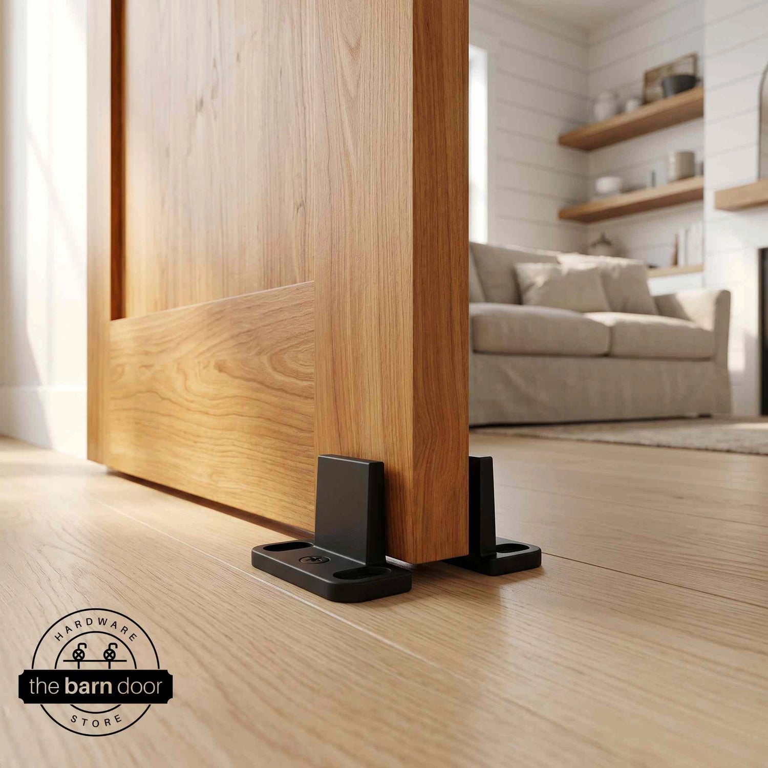 Matte black double clip floor guide installed at the base of a natural wood sliding barn door on light oak hardwood floors in a modern farmhouse living room