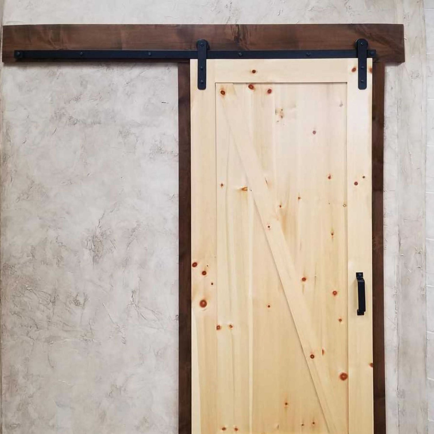 Farmhouse-style interior featuring a knotty pine barn door with a diagonal brace, hanging from a single track with Straight Strap rollers.