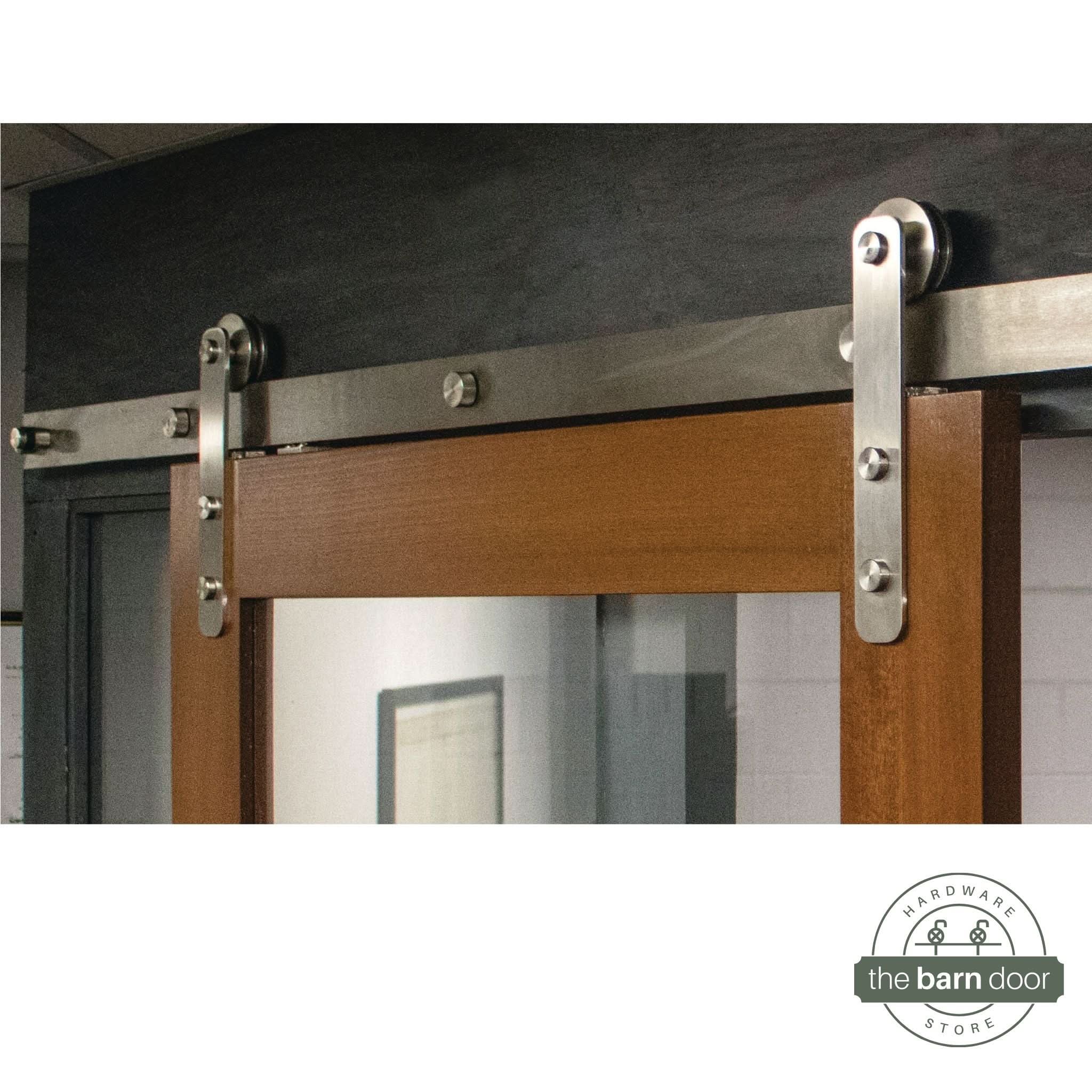 Straight Strap stainless steel barn door hardware kit installed on a single wood door, highlighting the sleek, minimalist roller design.