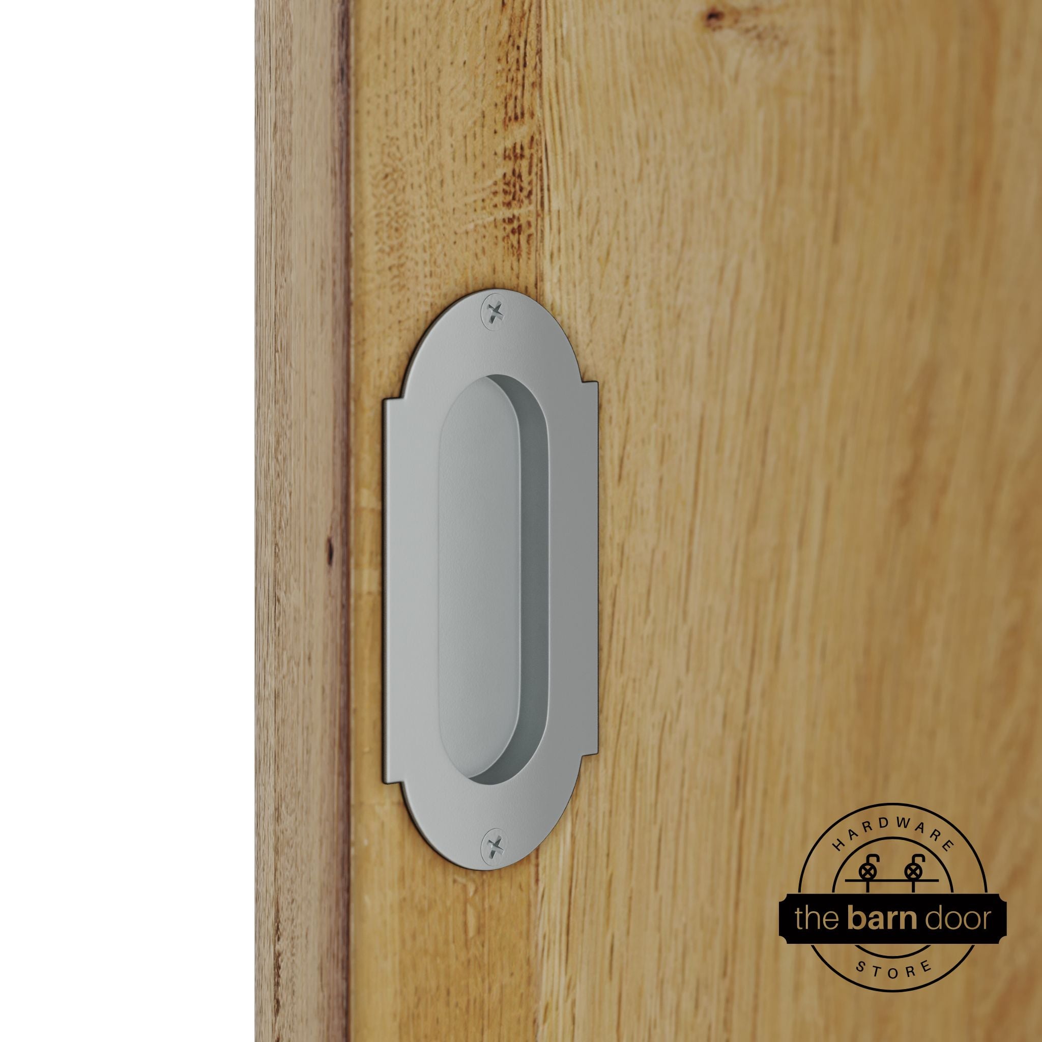 Silver metallic flush pull handle with full radius wings mounted on a light oak barn door, brushed silver finish with oval recessed grip and four mounting screws