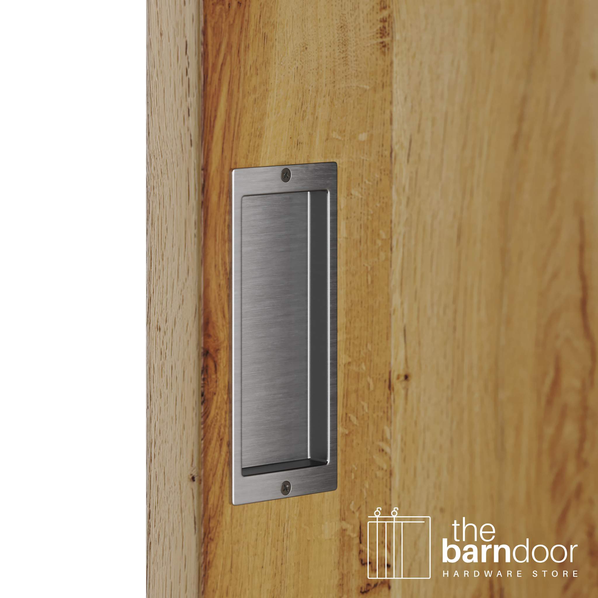 A close-up shot of a recessed rectangular flush pull handle in a stainless steel finish, installed on a light brown wooden barn door.