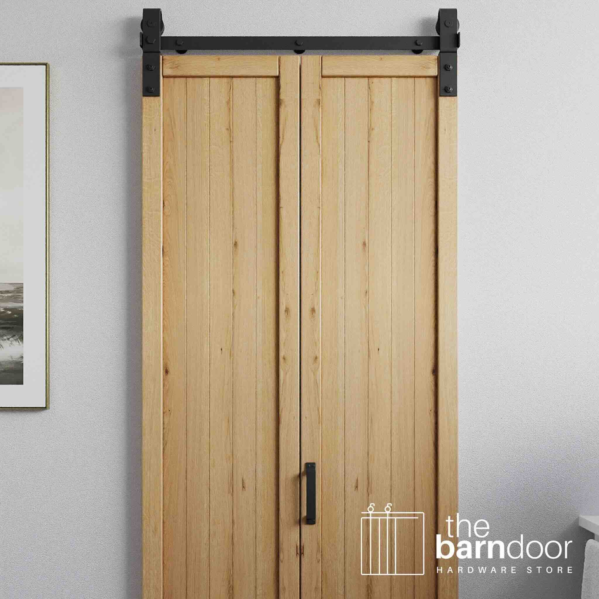 Wooden bifold sliding barn door with black hardware on a white wall, featuring 'the barn door hardware store' logo.