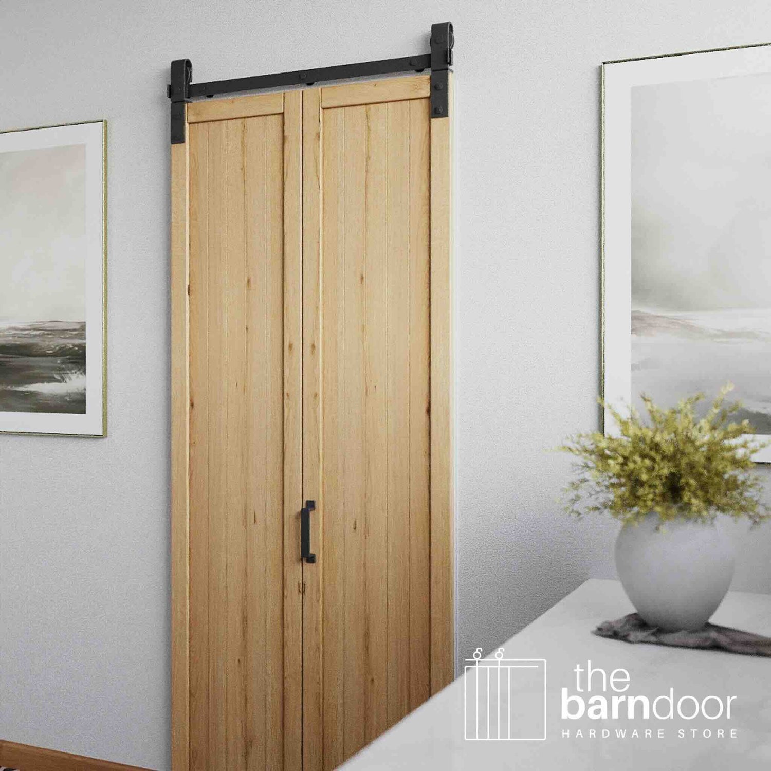 Wooden sliding bifold barn door with black hardware in a room with white walls and framed pictures.