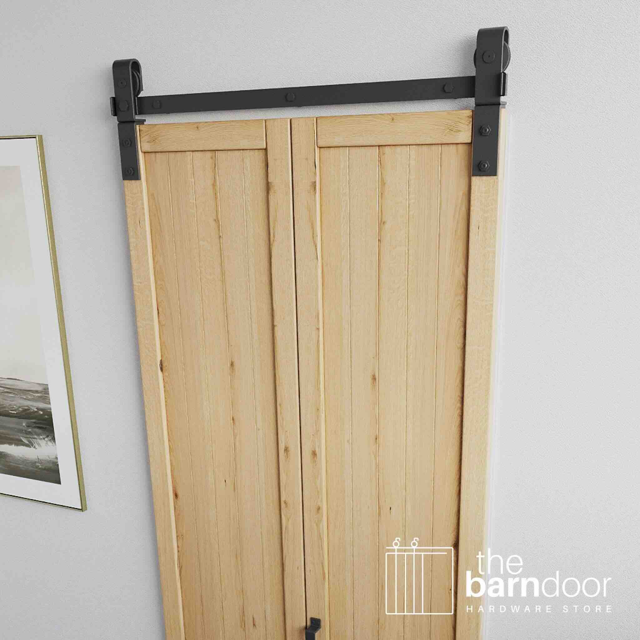 Wooden sliding bifold barn door with black hardware on a white wall, featuring 'the barn door hardware store' logo.