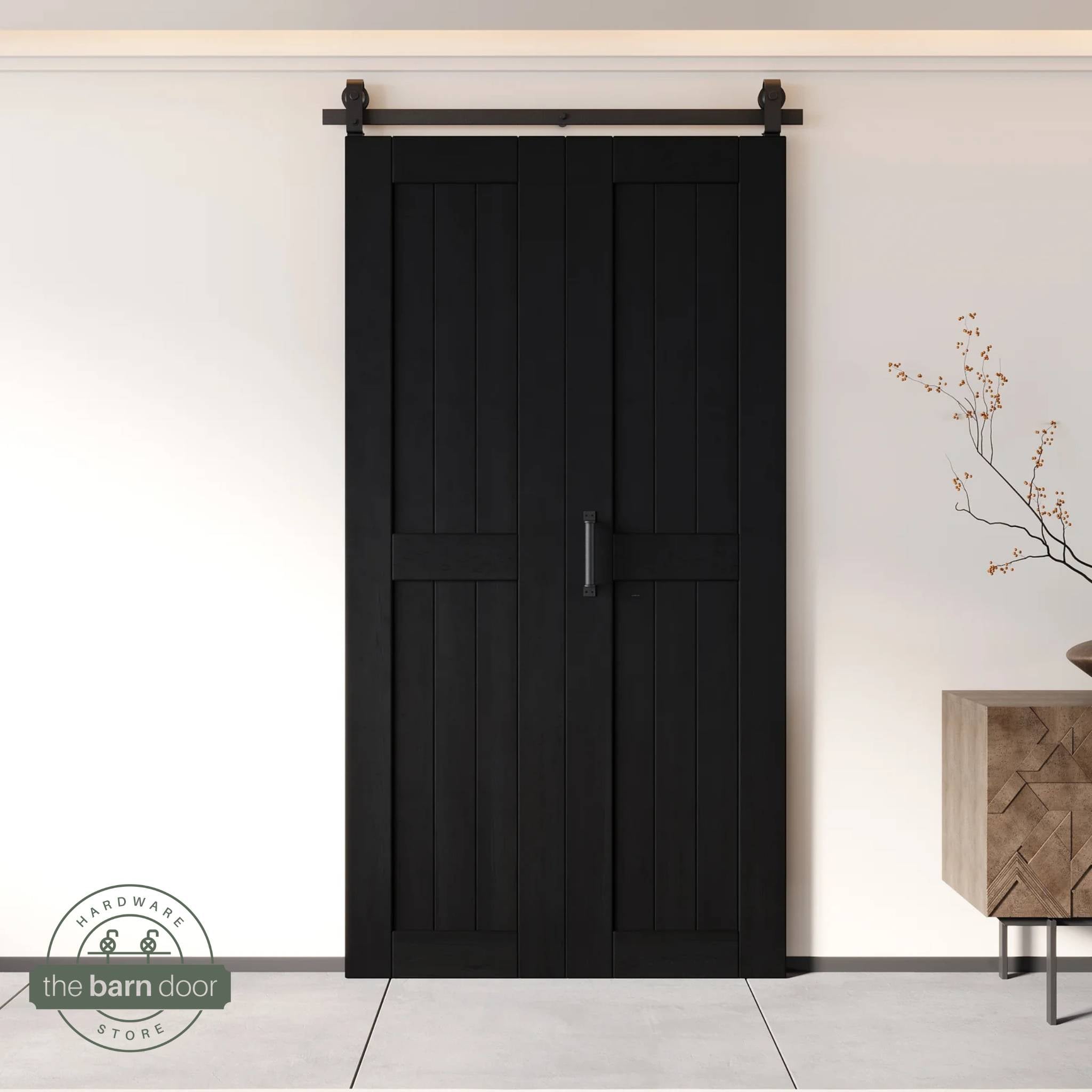 Two-panel bifold barn door in a black finish, installed and fully closed in a modern interior, showing the top-mount Matte Black track.
