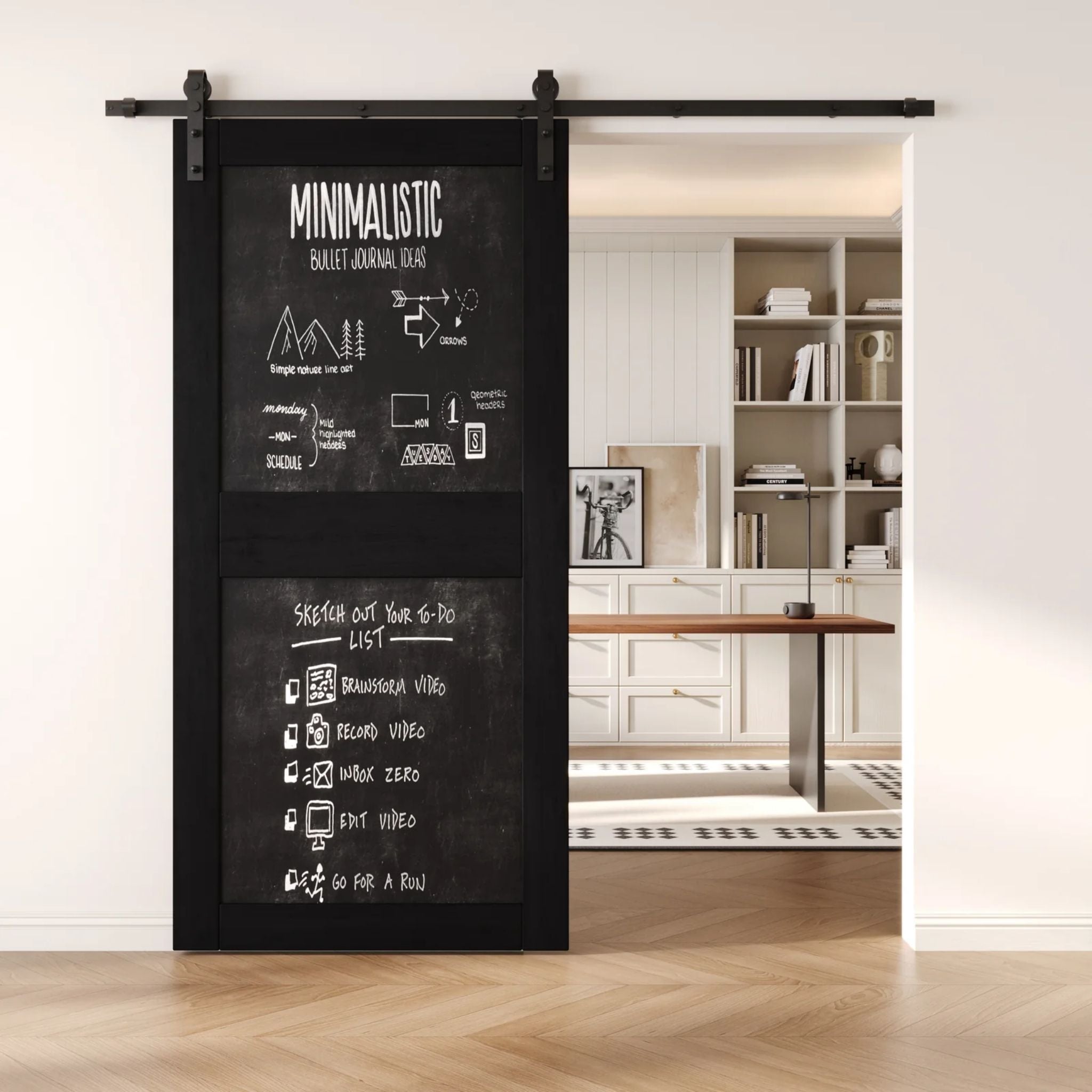 A black two-panel chalkboard barn door mounted on a sleek black sliding track, shown partially open to reveal a modern home office with built-in white shelving.