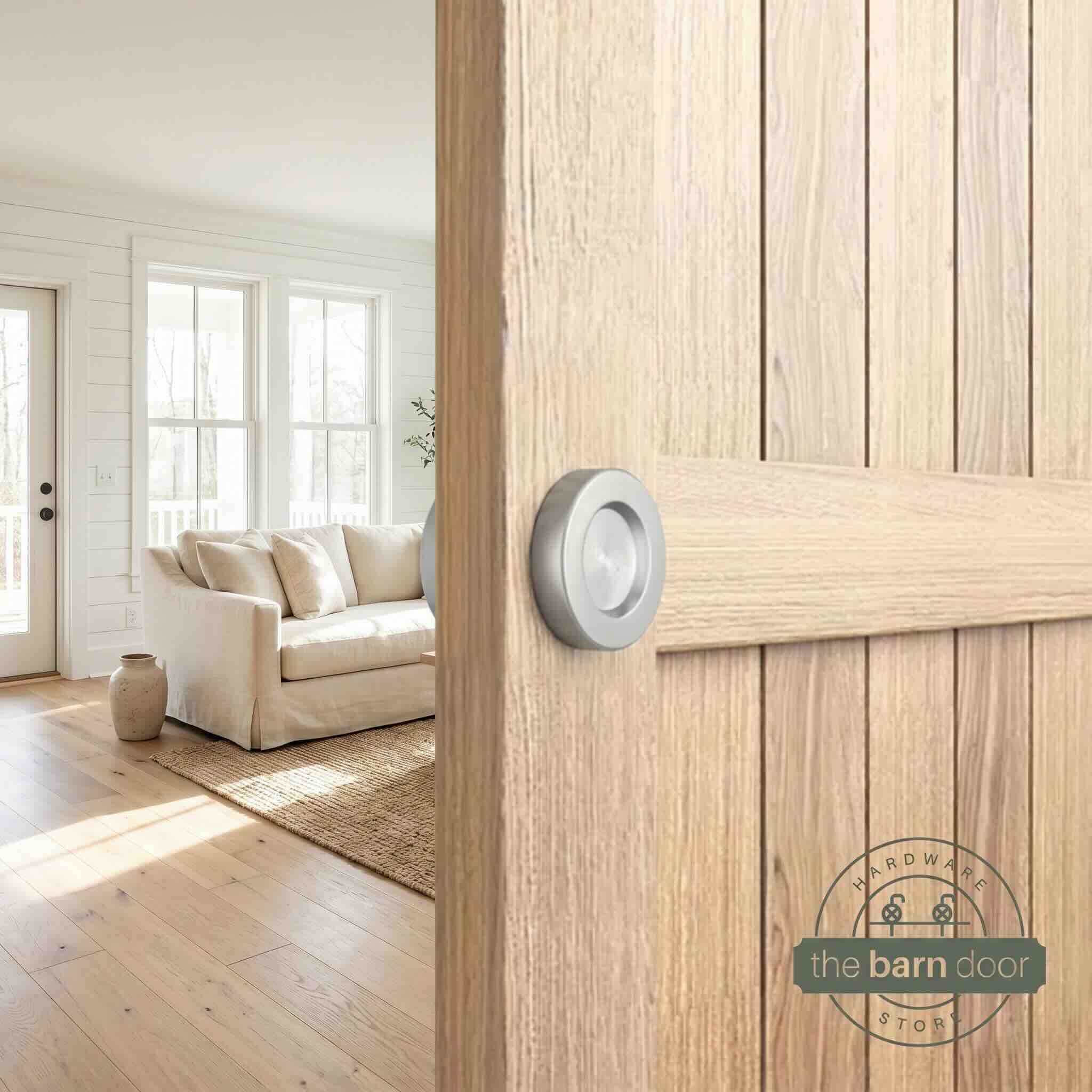 Stainless steel circular flush pull handle installed on a natural wood barn door in a living room setting