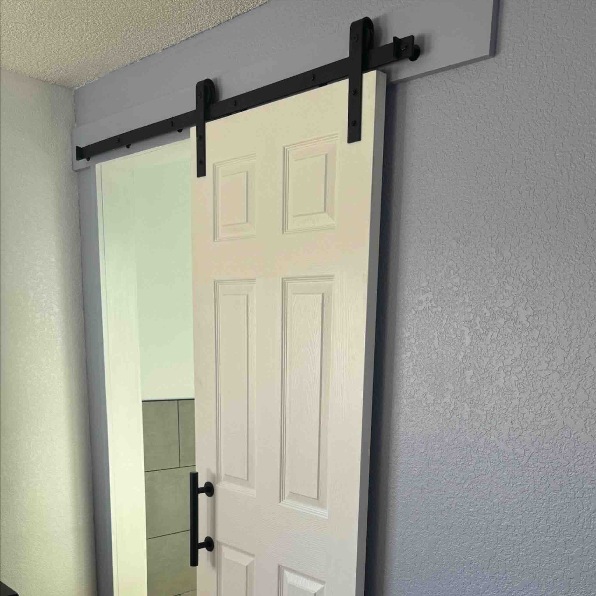 White sliding door with black hardware in a room with light gray walls.