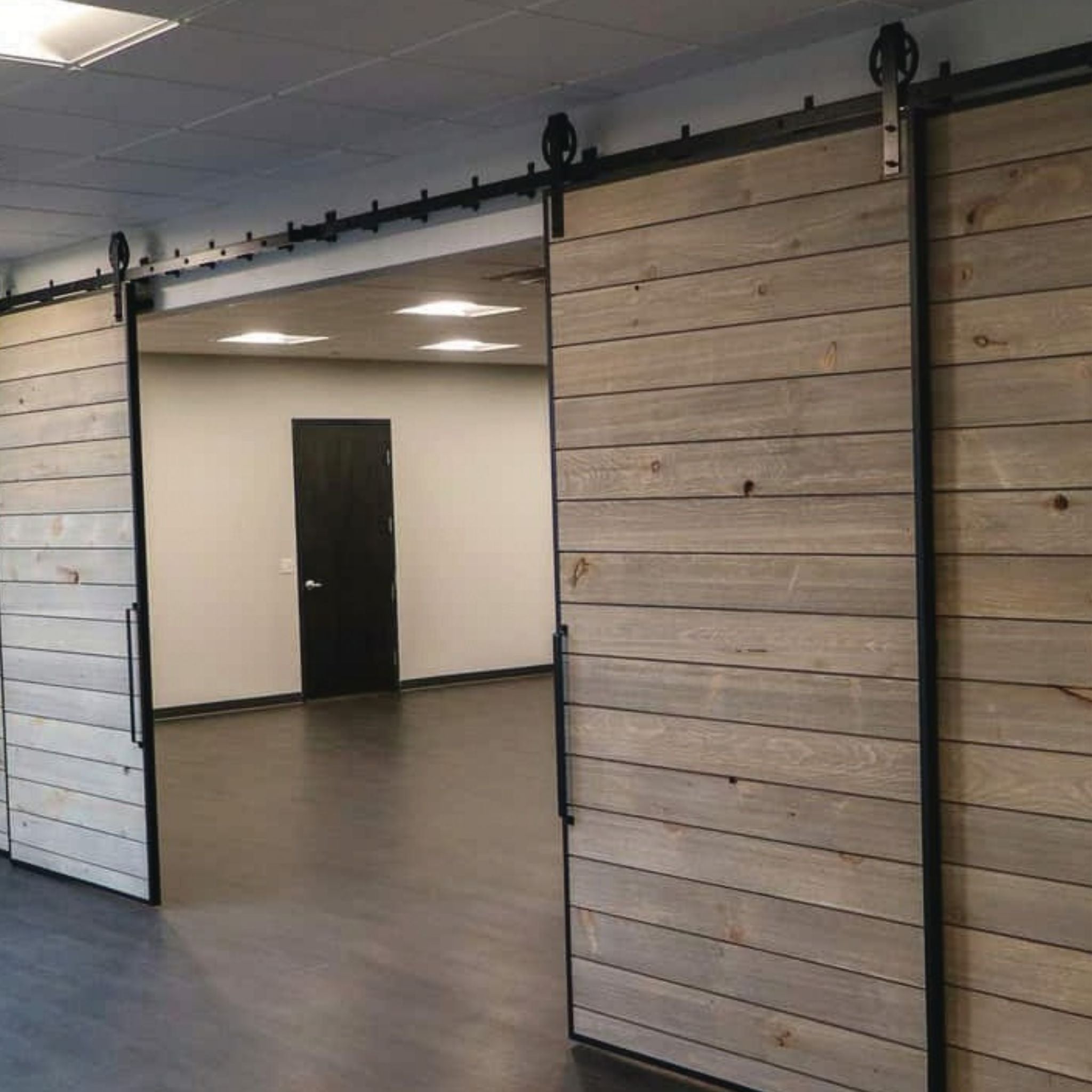 Two large sliding barn doors with Goldberg Brothers Edge Wrap and spoke wheel hardware installed on horizontal shiplap wood panels in a commercial space