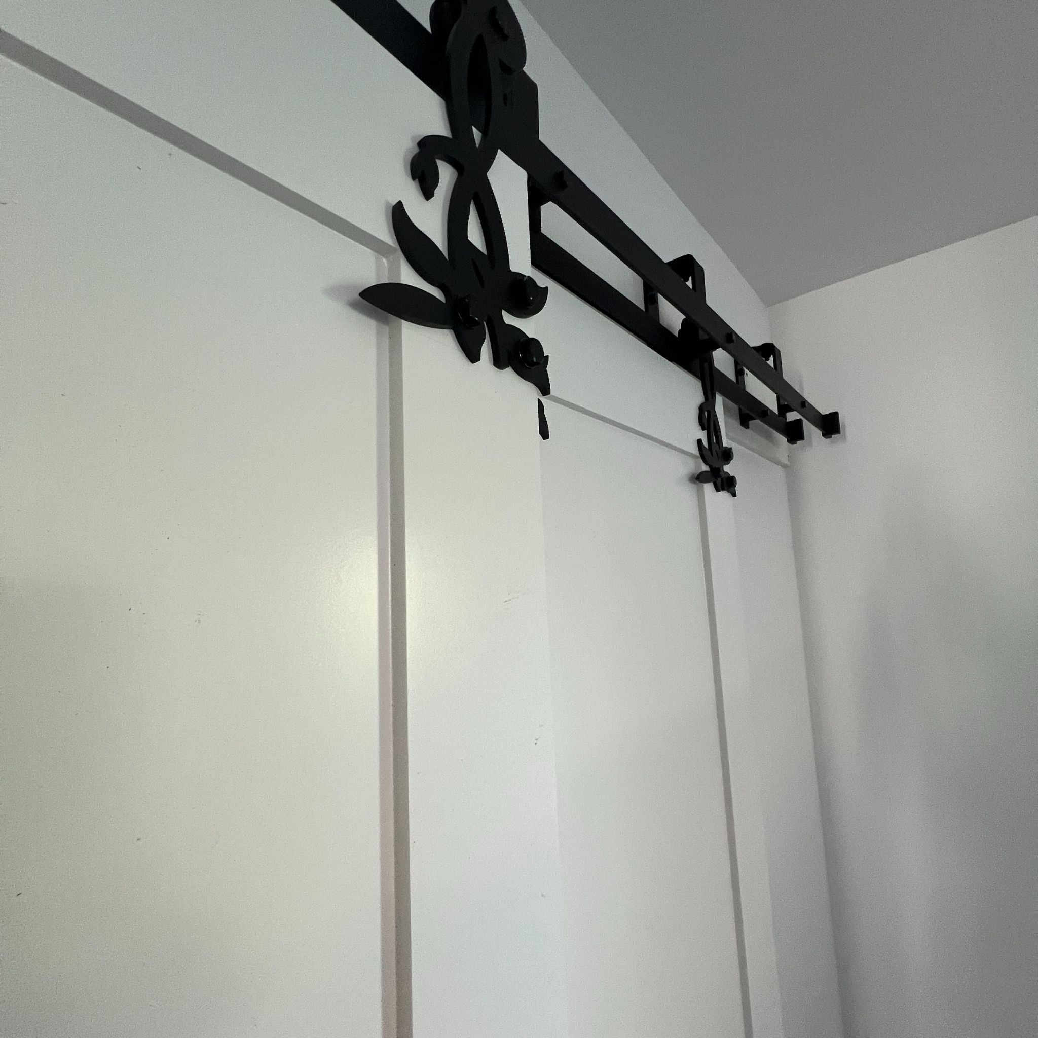 A close-up shot of ornate black sliding barn door hardware with decorative floral-inspired hangers mounted on white bypass closet doors.