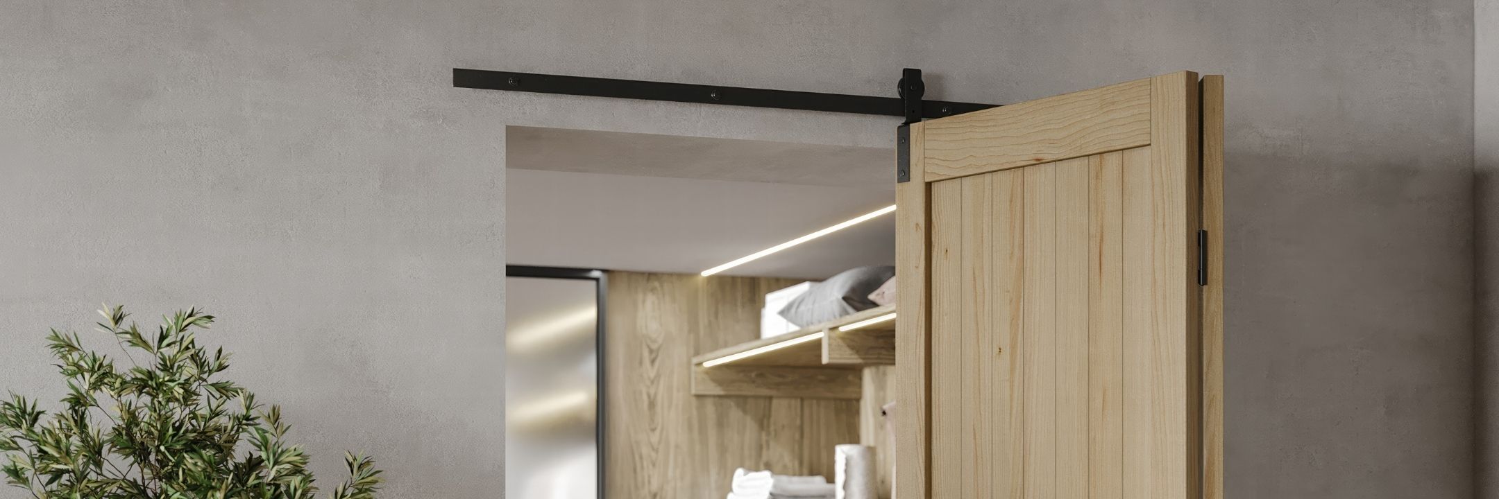 A panoramic view of a light wood bifold barn door system on a black track, open to reveal a lighted closet interior with wooden shelving.
