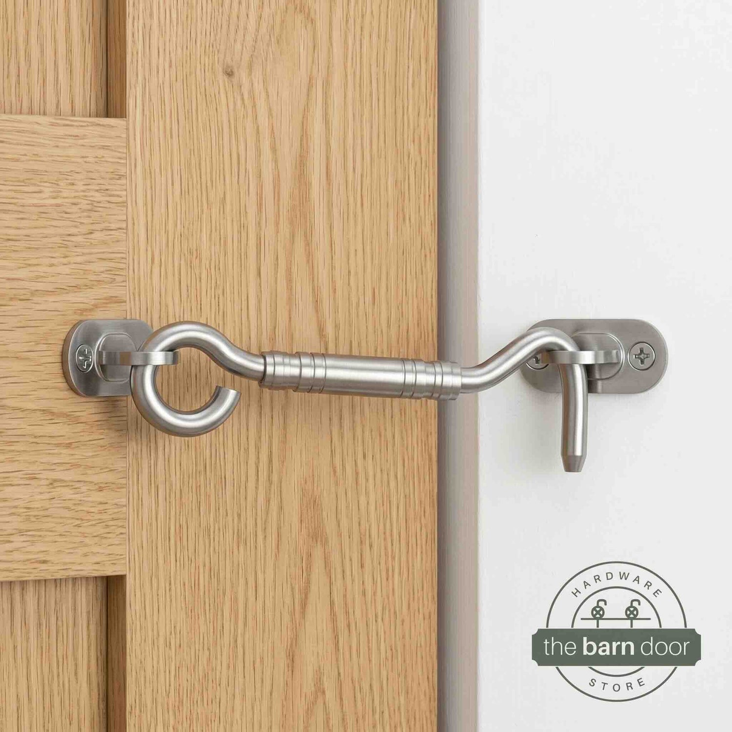 Stainless steel hook and eye barn door latch mounted on a white door securing it to the adjacent wall