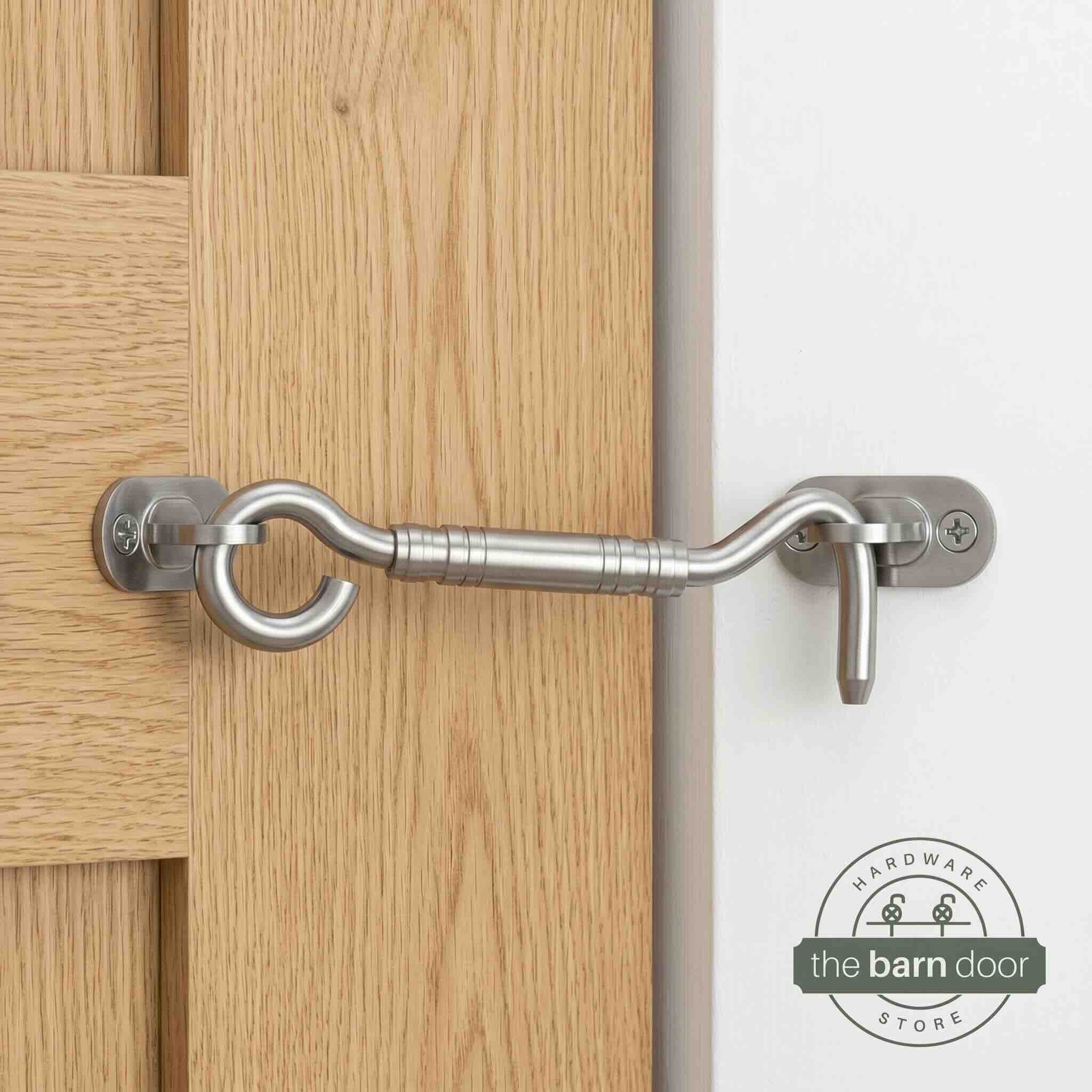 Stainless steel hook and eye barn door latch mounted on a white door securing it to the adjacent wall