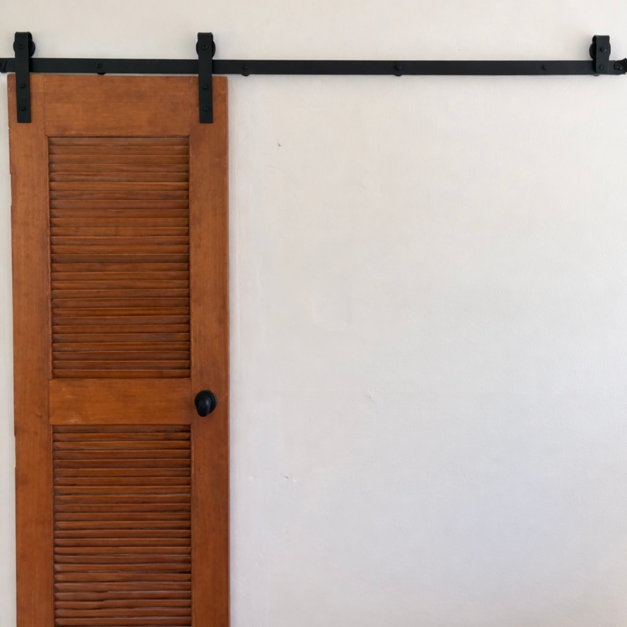 Wooden shutter door with black hardware on a white wall