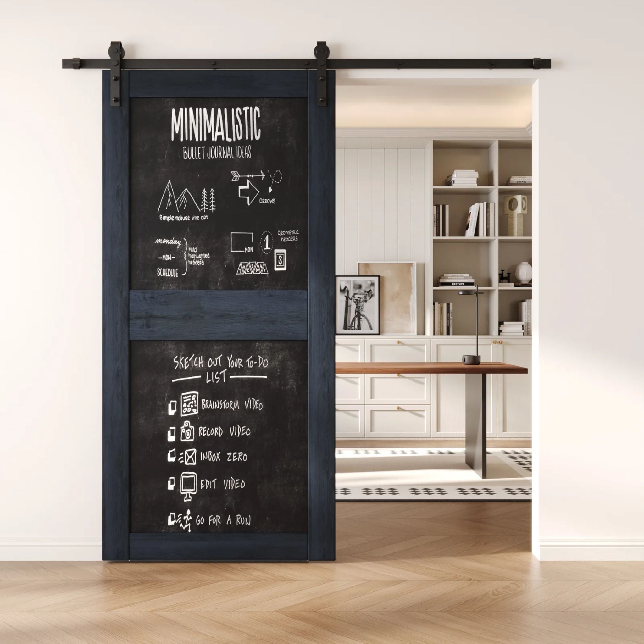 A navy two-panel chalkboard barn door mounted on a sleek black sliding track, shown partially open to reveal a modern home office with built-in white shelving.