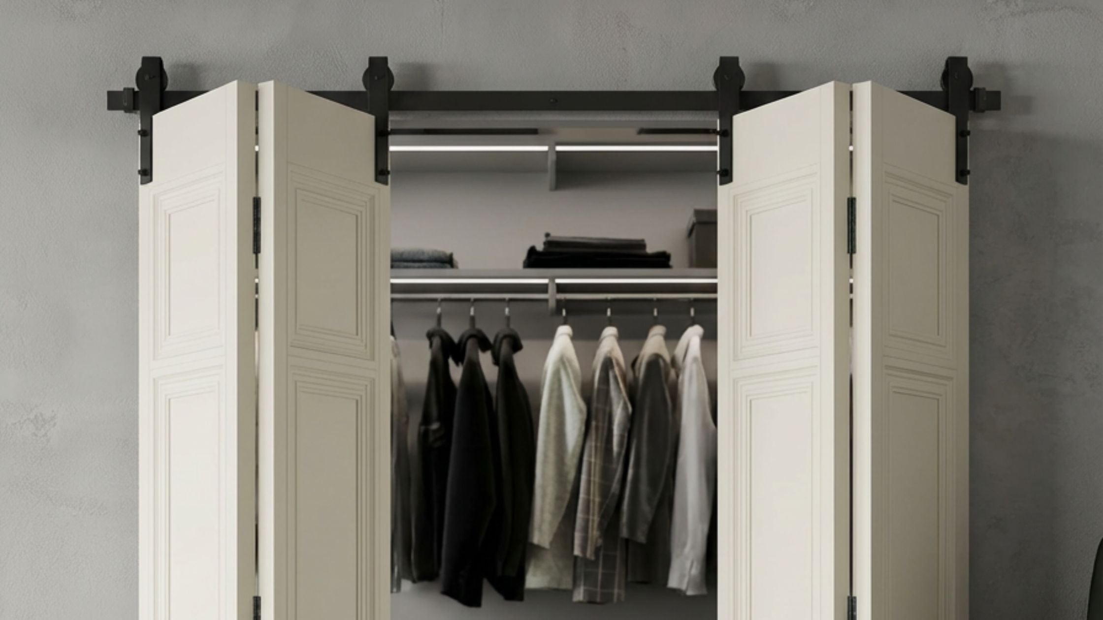 A pair of cream-colored bifold barn doors on a black metal sliding track, partially open to reveal an organized closet interior against a textured grey wall.