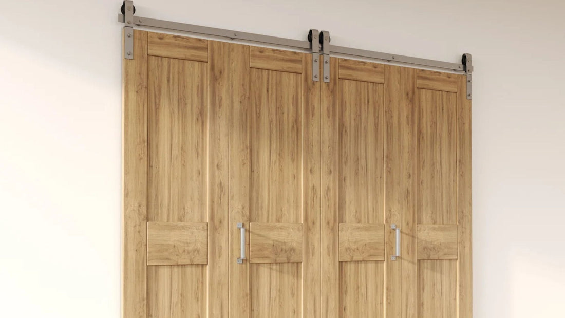 Four light wood bifold barn door panels with vertical planking and lower horizontal rails, installed on a brushed nickel top-mount sliding hardware track with matching bar handles.