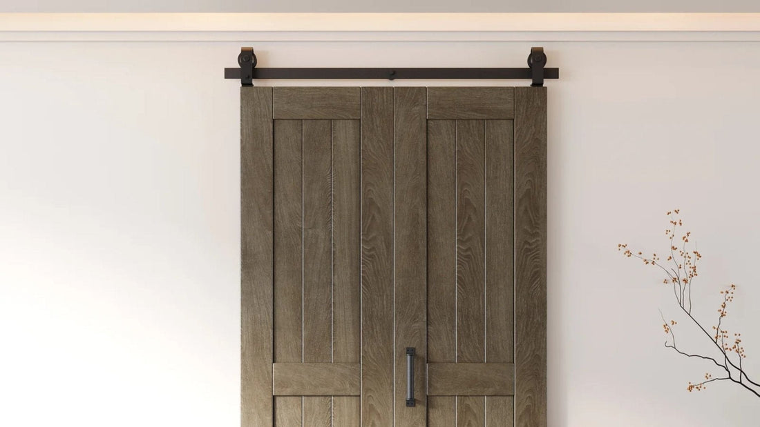 Close-up of matte black steel bypass barn door hardware, featuring large dual roller hangers and a rail mounted on a white painted brick wall. The wooden door surface is partially visible beneath the rail.