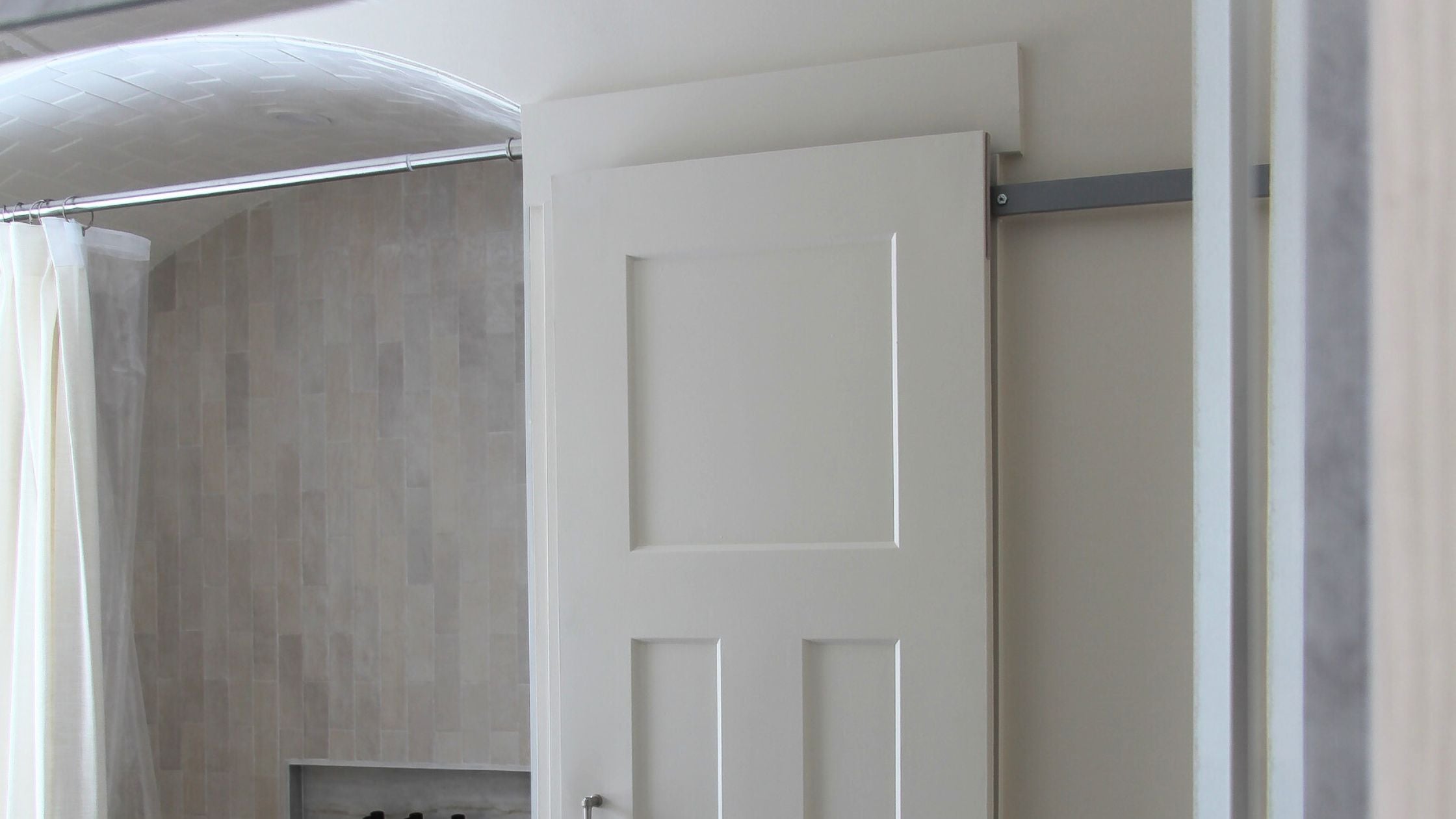 Hidden barn door hardware in a bathroom next to a shower.