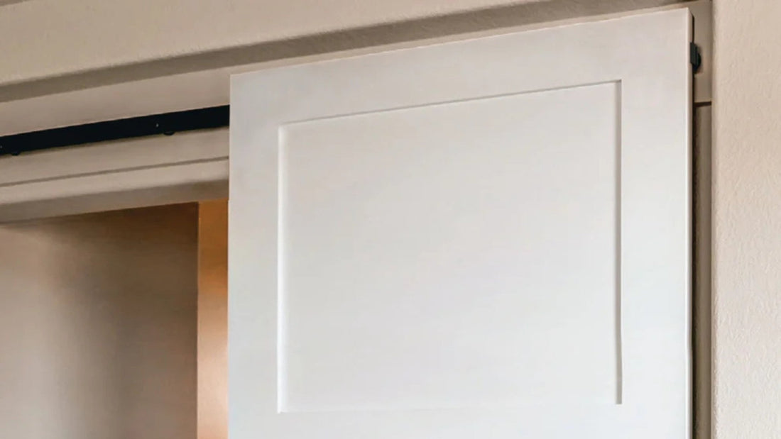 Detail shot of a white interior barn door installed with a hidden or concealed roller hardware kit. The black track is visible above the door panel, but the rollers are out of sight.