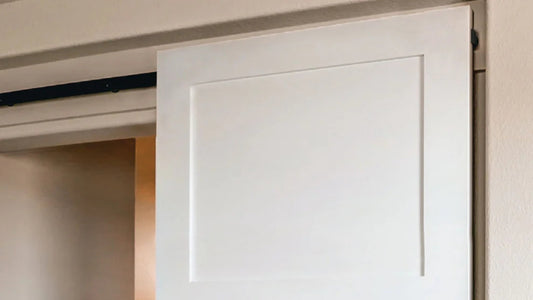 Detail shot of a white interior barn door installed with a hidden or concealed roller hardware kit. The black track is visible above the door panel, but the rollers are out of sight.