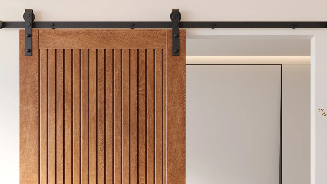 A light brown wood barn door with vertical fluting or slat panels is hung on a straight black sliding hardware track.