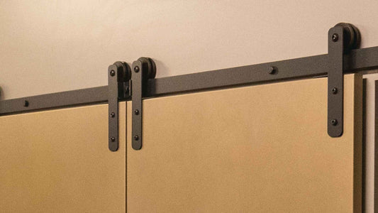 Close-up of mini barn door hardware in black, installed on a two-panel cabinet or media console door, showing the small rollers and track