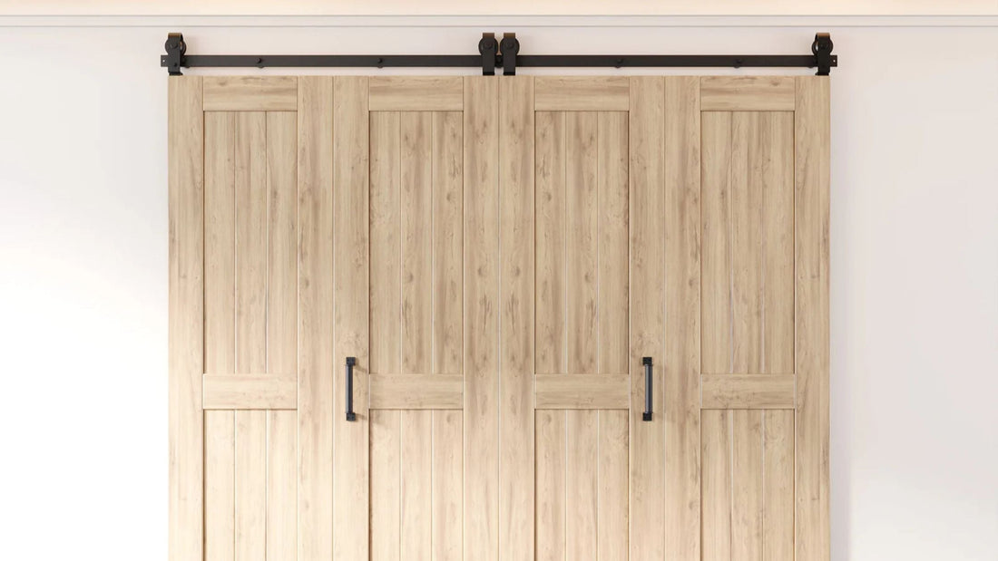 Four light-colored pine wood bifold barn door panels with a lower rail design, installed on a single black sliding hardware track with black vertical handles.