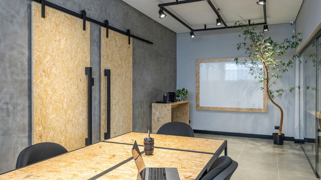 Modern industrial office with barn doors on a concrete wall, black sliding hardware, matching table, whiteboard, and a potted tree.