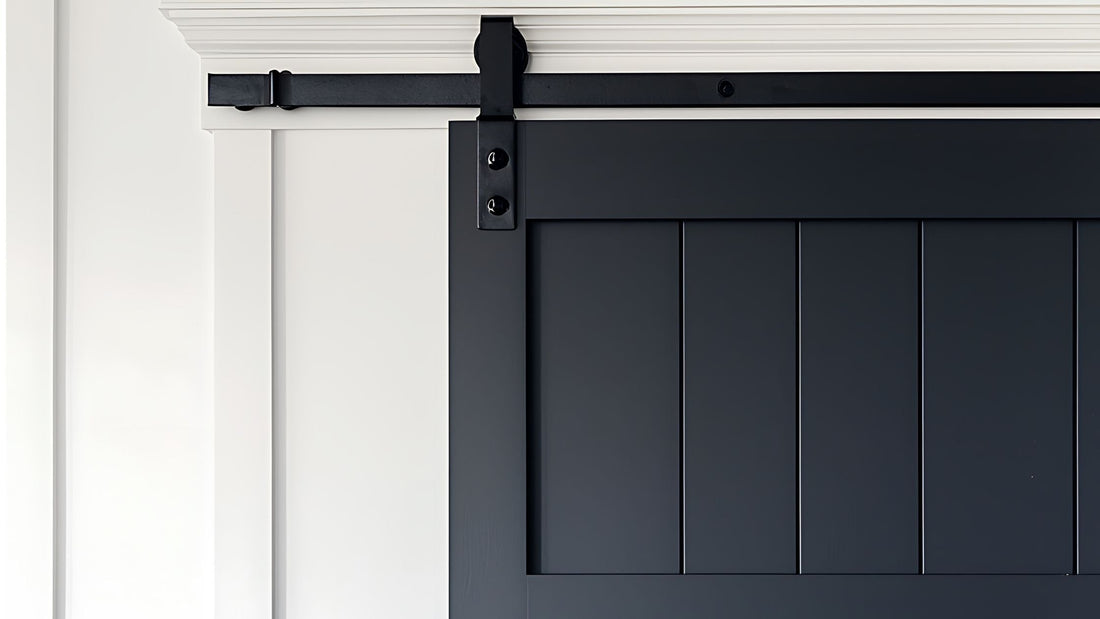 Close-up of a black vertical plank barn door with a shaker frame, installed with simple black roller sliding hardware against a white wall and crown molding trim.