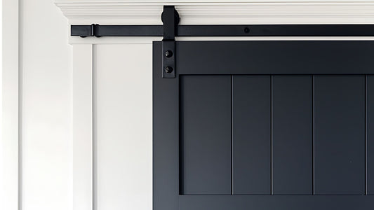 Close-up of a dark navy or black shaker-style barn door with vertical plank panels, hung on simple black rolling hardware against a white wall with decorative trim.