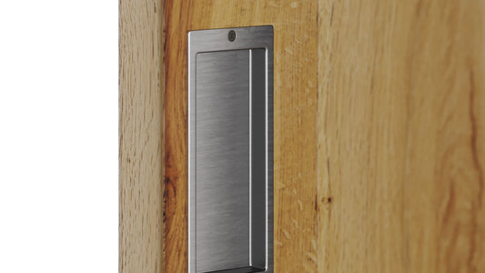 Close-up of a modern, rectangular brushed stainless steel flush pull handle recessed into a light oak wood barn door.