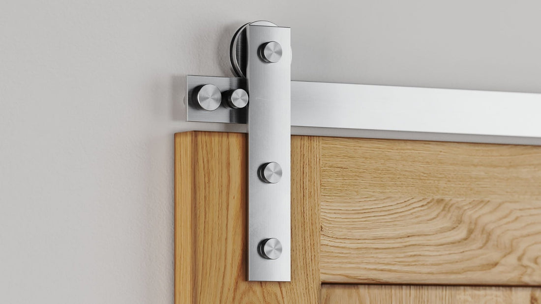 Close-up of modern barn door hardware featuring a brushed stainless steel flat track and hanger mechanism attached to a light oak wood door panel.