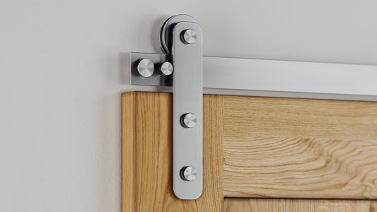 Close-up of modern, brushed stainless steel flat track sliding door hardware installed on a light oak wood door panel against a white wall.