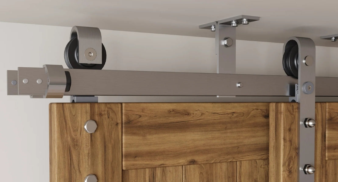 A close-up of a ceiling mount sliding barn door hardware kit in a brushed steel finish, highlighting the robust top mount rollers and track system.