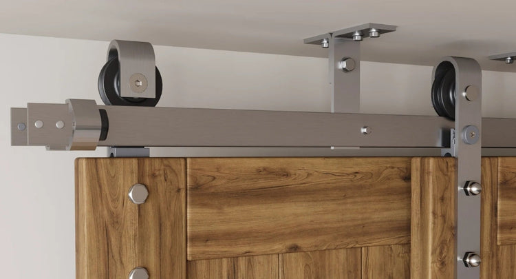 A close-up of a ceiling mount sliding barn door hardware kit in a brushed steel finish, highlighting the robust top mount rollers and track system.