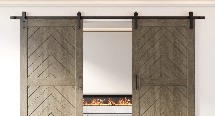 A close-up of two wood barn doors with a chevron pattern, featuring a classic J-strap style double sliding barn door hardware kit in a matte black finish.