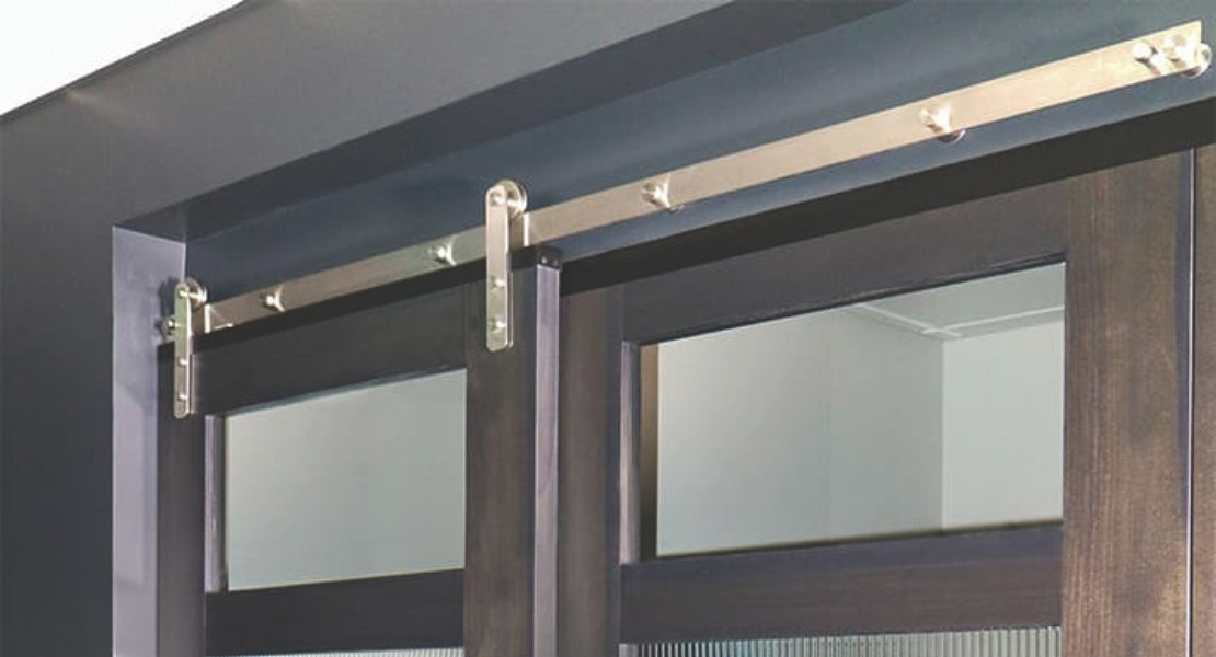 A close-up showcasing the durable construction of our stainless steel barn door hardware kit on two wood and glass doors, highlighting the sleek J-strap style rollers.