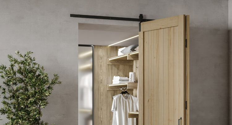 A close-up of a two-door bifold barn door system in a closet, showcasing the hardware's functionality as a light wood door is partially folded to reveal a shelving unit inside.