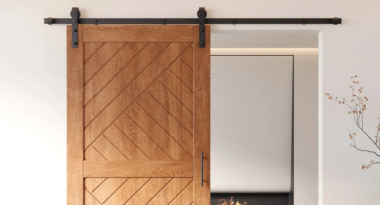 A close-up of a rustic wood barn door with a chevron pattern, featuring a classic J-strap style single track hardware kit in a matte black finish.