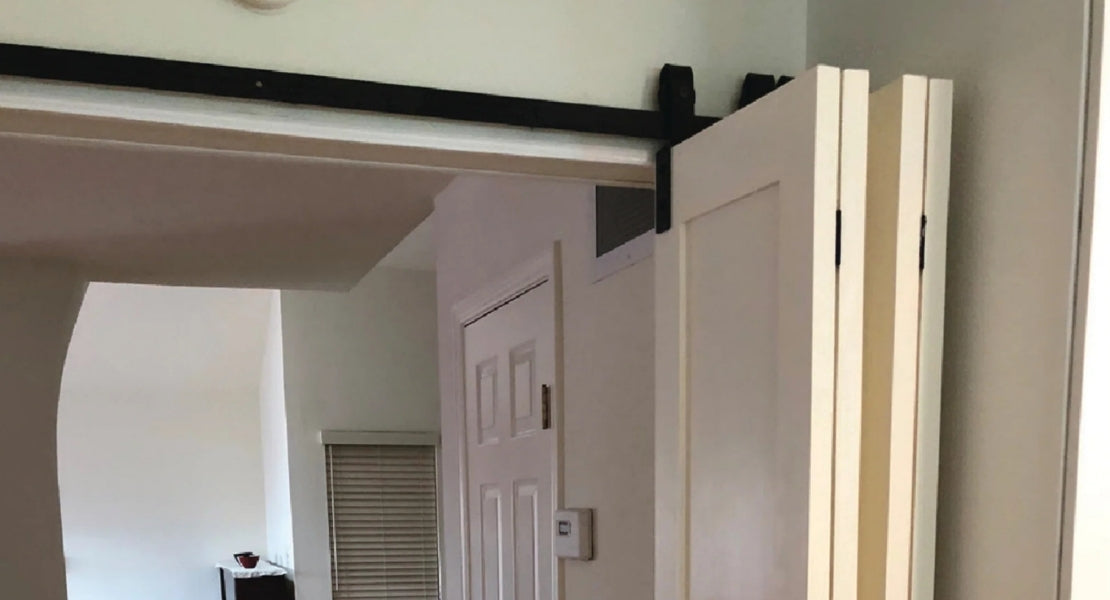  A close-up of a white bifold barn door system in a hallway, showcasing the hardware's functionality as the doors are partially folded.