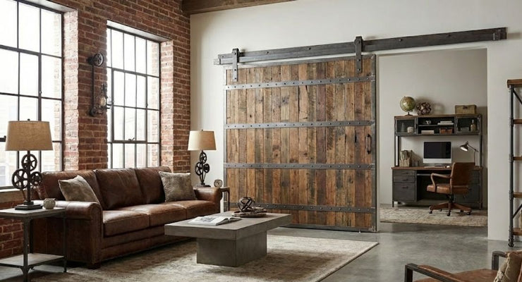 A heavy-duty industrial barn door made of dark, distressed wood slides on a raw steel track with J-strap hangers.