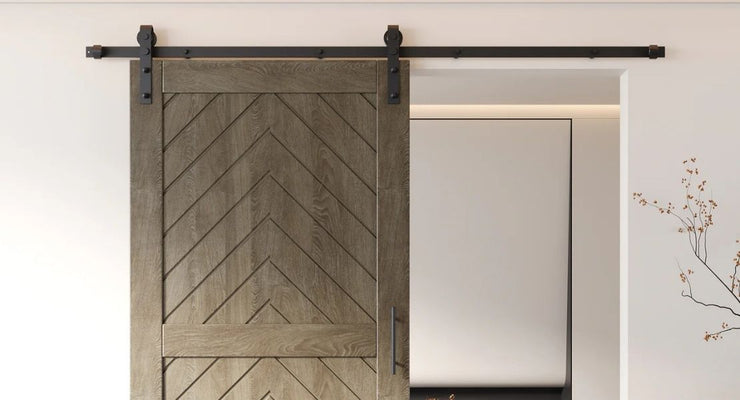 A chic modern barn door featuring a chevron wood grain pattern in a grey-brown finish, hanging on a black track in a minimalist white room.