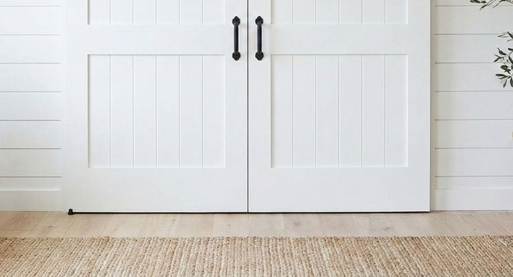 A pair of white paneled bifold barn doors hanging from a black track with J-strap rollers against a plain white background.