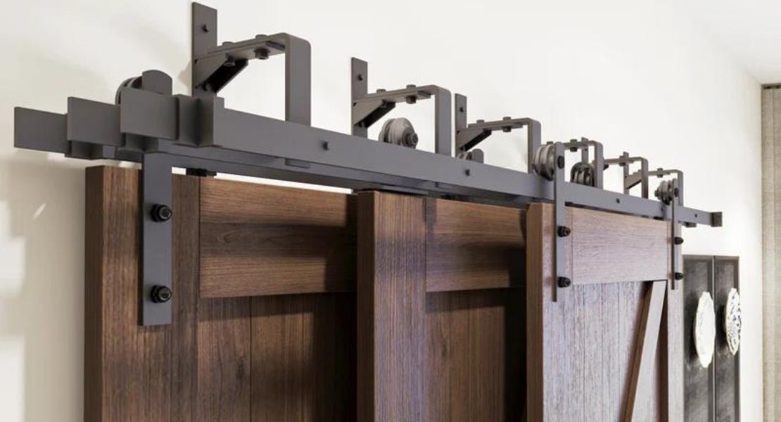 A close-up of a three-door triple bypass barn door system with dark wood doors, showcasing a visible top-mount track and robust hardware in a matte black finish.