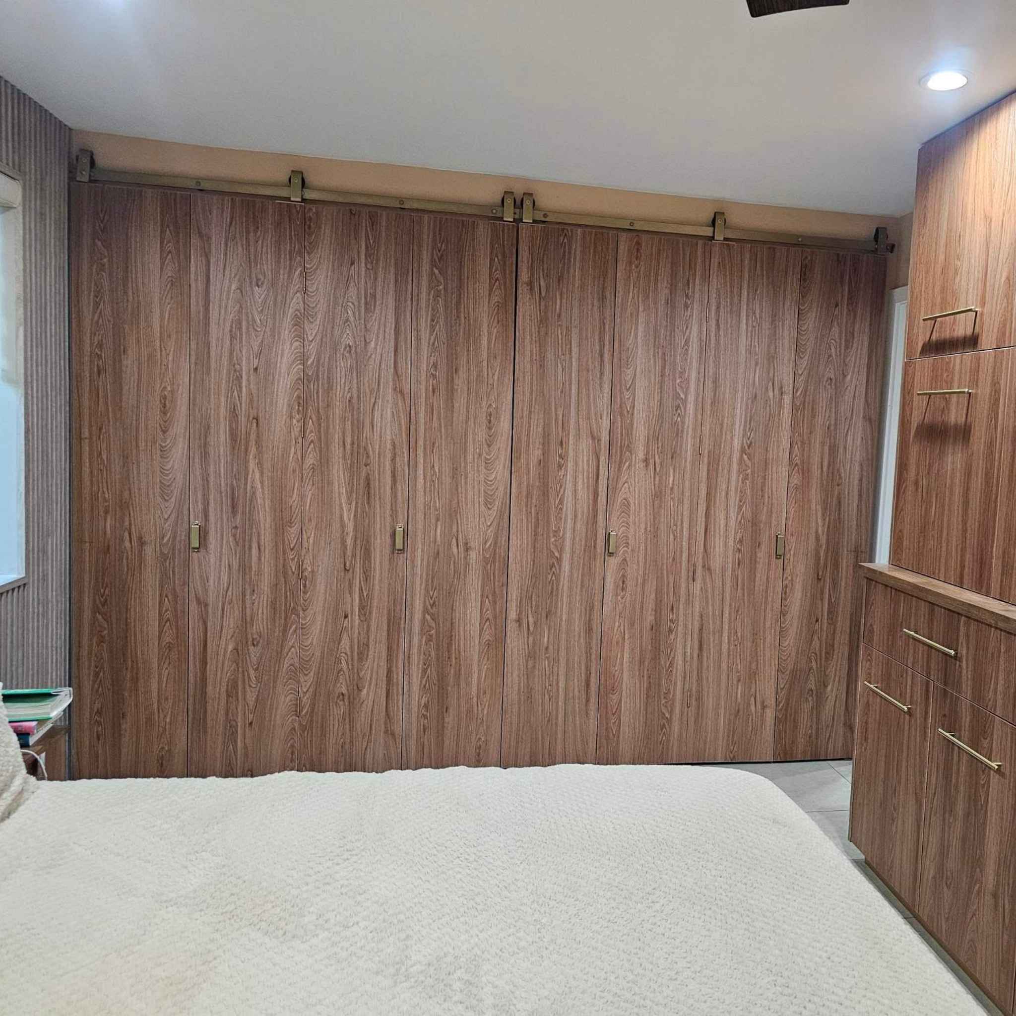 A customer install of an 8-door bi-parting bifold barn door system in a bedroom, featuring J Top Mount hardware in a Jacobs Gold finish.
